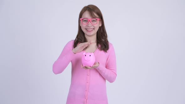 Young Happy Asian Nerd Woman Holding Piggy Bank and Giving Thumbs Up