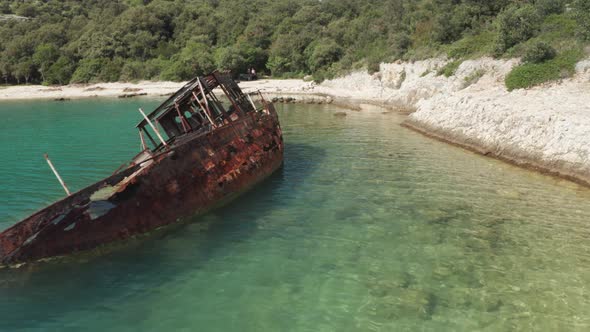 Close up shot of a rusted ship wrecked on the side of a beautiful Croatian beach. Aerial shot.