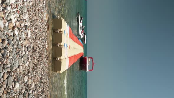 Floating plastic pontoon on pebble beach with moored small yacht and jet bikes, vertical video. 