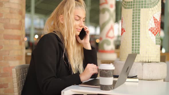 Woman talking on smartphone while working with laptop in cafe