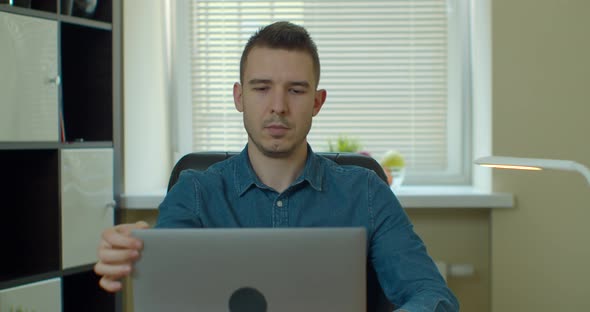 Young Man Sitting at His Desk at Home, Opens and Starts Using Laptop.