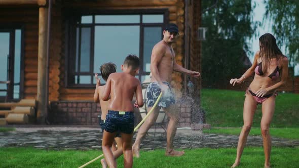 Family in the Backyard of a Country House in the Summer Relax Playing with Water and Hosing