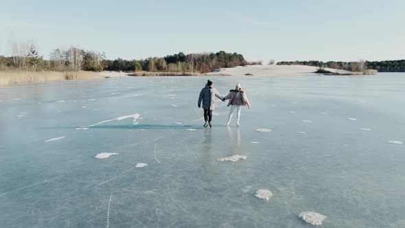 Aerial Shot of Couple Skating on a Blue Frozen Lake in Beautiful Sunny Landscape