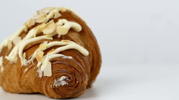 Rotation of a baked croissant with cream and almonds on a white plate.