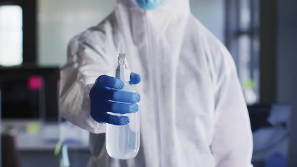 Health worker wearing protective clothes and face mask spraying disinfectant at modern office