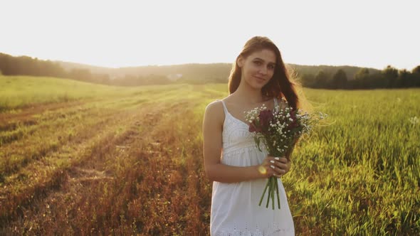 Young Woman Standing in a Meadow with Bouquet of Wild Flowers on Summer Evening