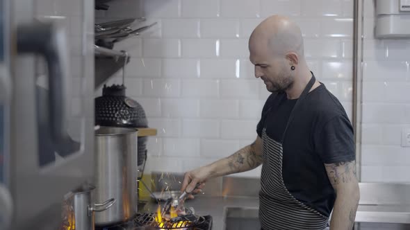 White Male Chef Moves Charcoal on Grill Grate on Gas Stove Side View