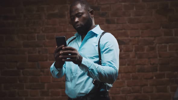 Confident African Detective with Holsters Using Smartphone Isolated on Red Brick Wall Background