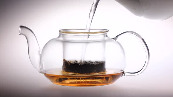 Boiling Water Is Poured Into Glass Teapot with Tea Leaves