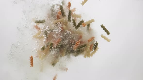 Italian Rotini Macaroni Pasta Falling Into Boiled Water. Multi-colored Fusilli Pasta. Slow Motion