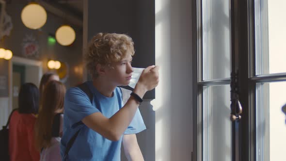 Side View of Teen Schoolboy Putting Off Safety Mask and Looking Out of Window in School Corridor