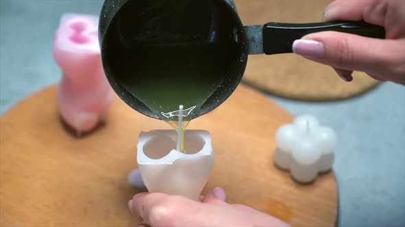 A woman occupied with hand made candles production, pouring melted wax into the mold. Slow motion