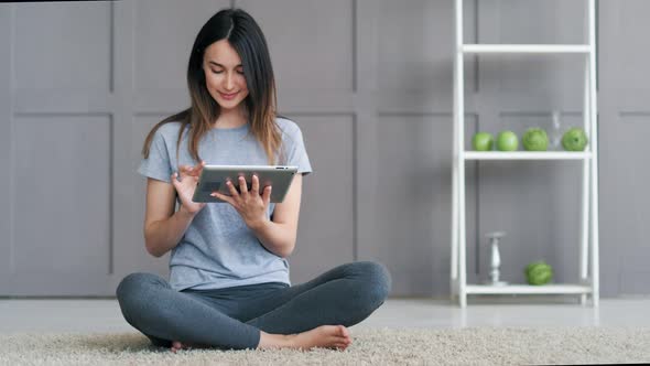 Young Happy Woman Sitting on the Floor and Using Tablet Computer at Home