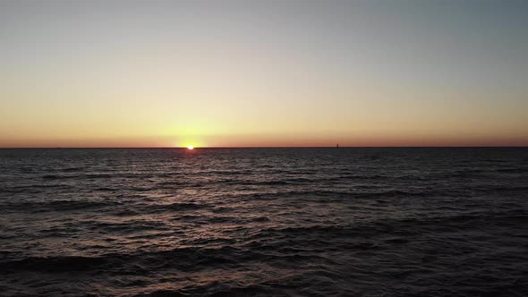 Red Sun Sets Over Ocean Sea with Waves and Small Black Yacht Boat in Horizon. Sun Road from Sunset