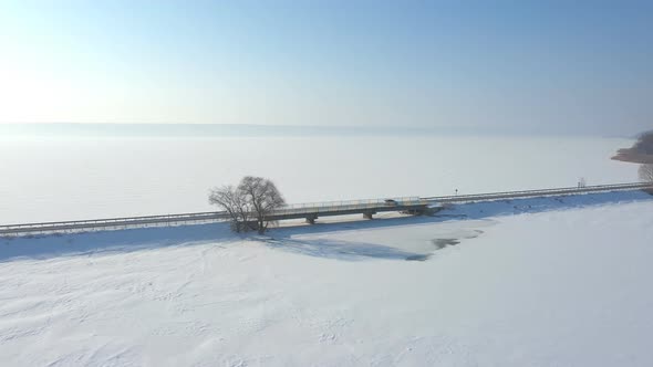 Aerial Shot of White Car Riding Through Snow Covered Road Near a Frozen Lake