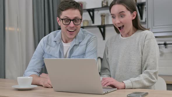 Excited Young Couple Celebrating Success on Laptop at Home 