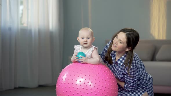 Happy Mother and Cute Baby Girl Smiling at Camera, Playing With Balls at Home