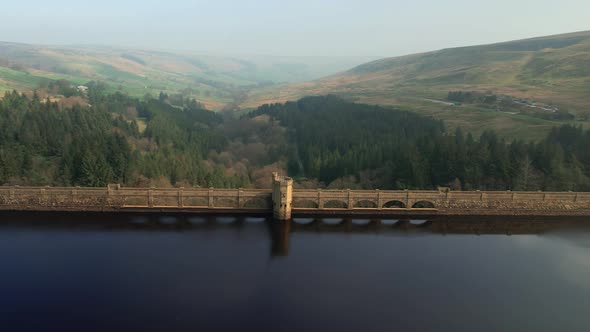 Aerial view passing Scar house reservoir landmark flying out towards vibrant Yorkshire valley countr