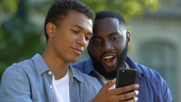 African-American Teenager Showing Photos on Smartphone to Smiling Man, Family