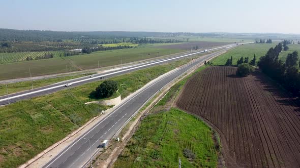 aerial, almost static, forward drone shot of two highways, surrounded by fields, green grass, trees,