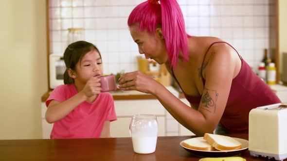 Young mother and kid daughter having breakfast in kitchen