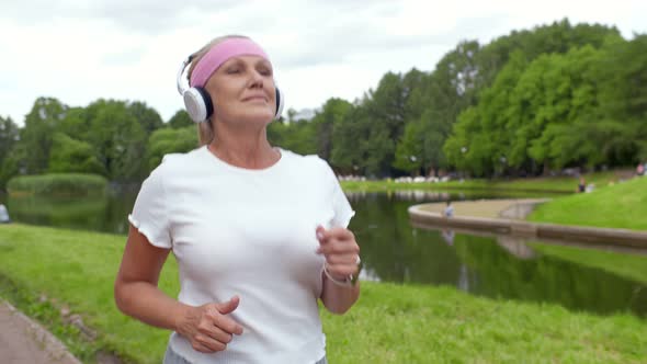 Portrait of Cheerful Mature Lady Listening To Music Jogging in Summer Park.