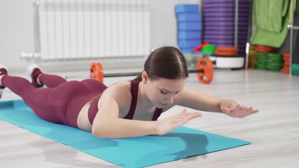 a Beautiful and Slender Woman in a Burgundy Tracksuit Exercises on a Mat