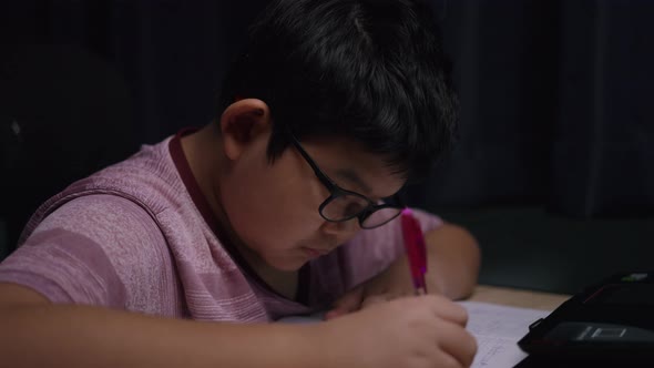 Asian boy is writing a book with a laptop