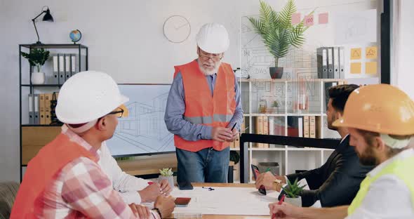 Engineer in Helmet and Vest Explaining Building Project Depikted on Digital Display and Glass Wall