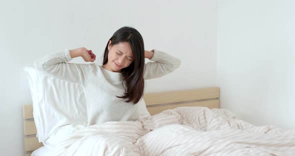 Woman feeling shoulder pain and sitting on bed