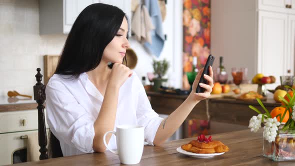 Young Woman Using Smartphone In The Kitchen With Morning Coffee