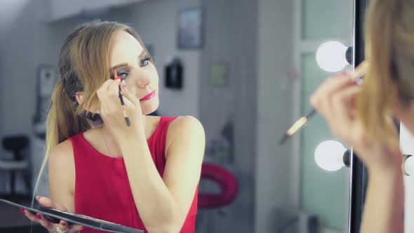 Mirror Reflection of Young Woman in Red Dress Painting Her Eyebrows