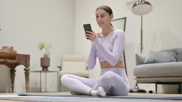Young Latin Woman Talking on Video Call on Smartphone While Sitting on Yoga Mat