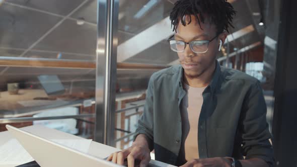 Young Black Man in Wireless Earphones Working on Laptop at Office Desk