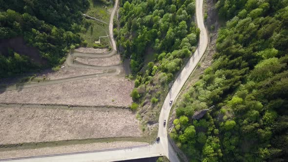 Aerial Top down shot of cars driving on road along reservoir with trees in the foreground