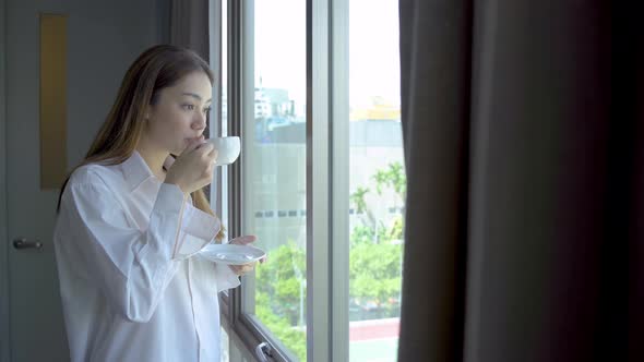 Young woman drinking hot coffee looking out window, Girl relaxing and enjoying