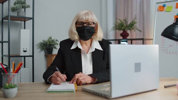 Senior Employee Wears Face Mask Works Alone From Home Office Sits at Desk Using Laptop Computer