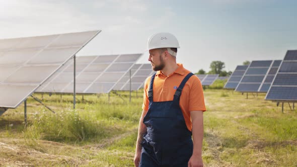 Industrial Man Engineer in Uniform Walking Through Solar Panel Field for