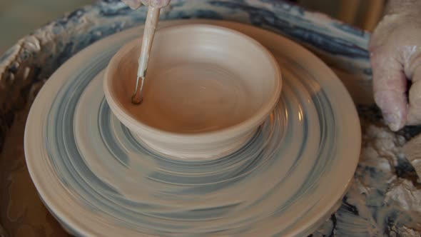 Seamless Loop of Ceramic Bowl Rotating on Potter's Wheel and Ceramist's Hand Decorating It