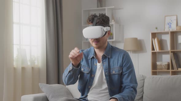 Young Caucasian Man Wearing Virtual Reality Glasses at Home in the Living Room