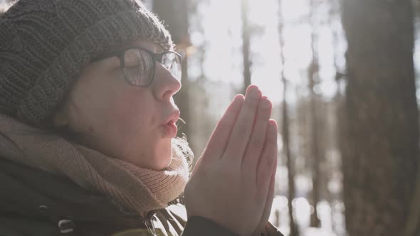 Woman with Freckles in Glasses Warms Hands with Warm Breath in the Forest