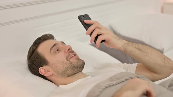 Video Chat on Smartphone By Young Man Laying in Bed