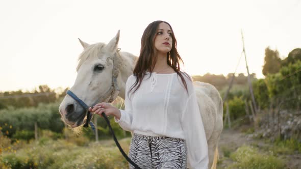 Beautiful Girl in White Dress Walks with Her Horse in the Private Countryside