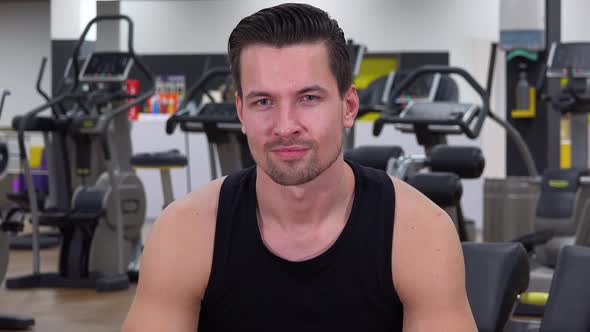 A Young Fit Man Shows a Thumb Up To the Camera and Nods in a Gym - Closeup