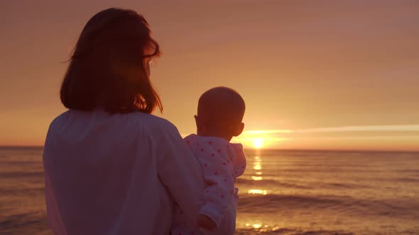 Young mother hugs her baby on the background of the sea