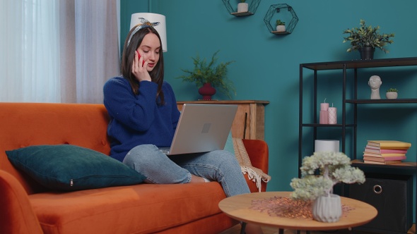 Cheerful Young Brunette Woman Sitting on Sofa Using Laptop Pc Talking on Mobile Phone at Home Office