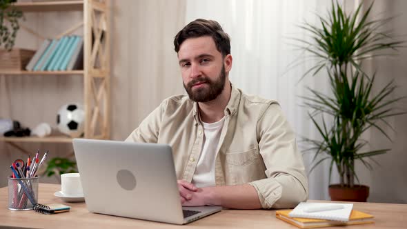 Handsome Bearded Man Uses Laptop While Sitting at the Table in Home Office