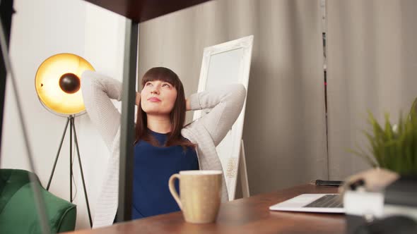 White Brunette Woman Sitting By Desk Resting and Stretching Arms Going Back to Work on Laptop