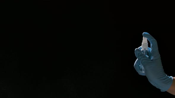 A Hand in a Blue Protective Glove Sprays an Antiseptic on a Black Background. Spray Disinfection