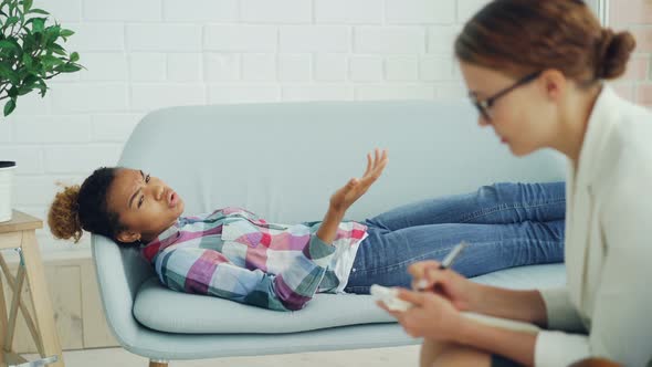 Depressed African American Girl Is Talking To Psychologist Lying on Sofa and Speaking